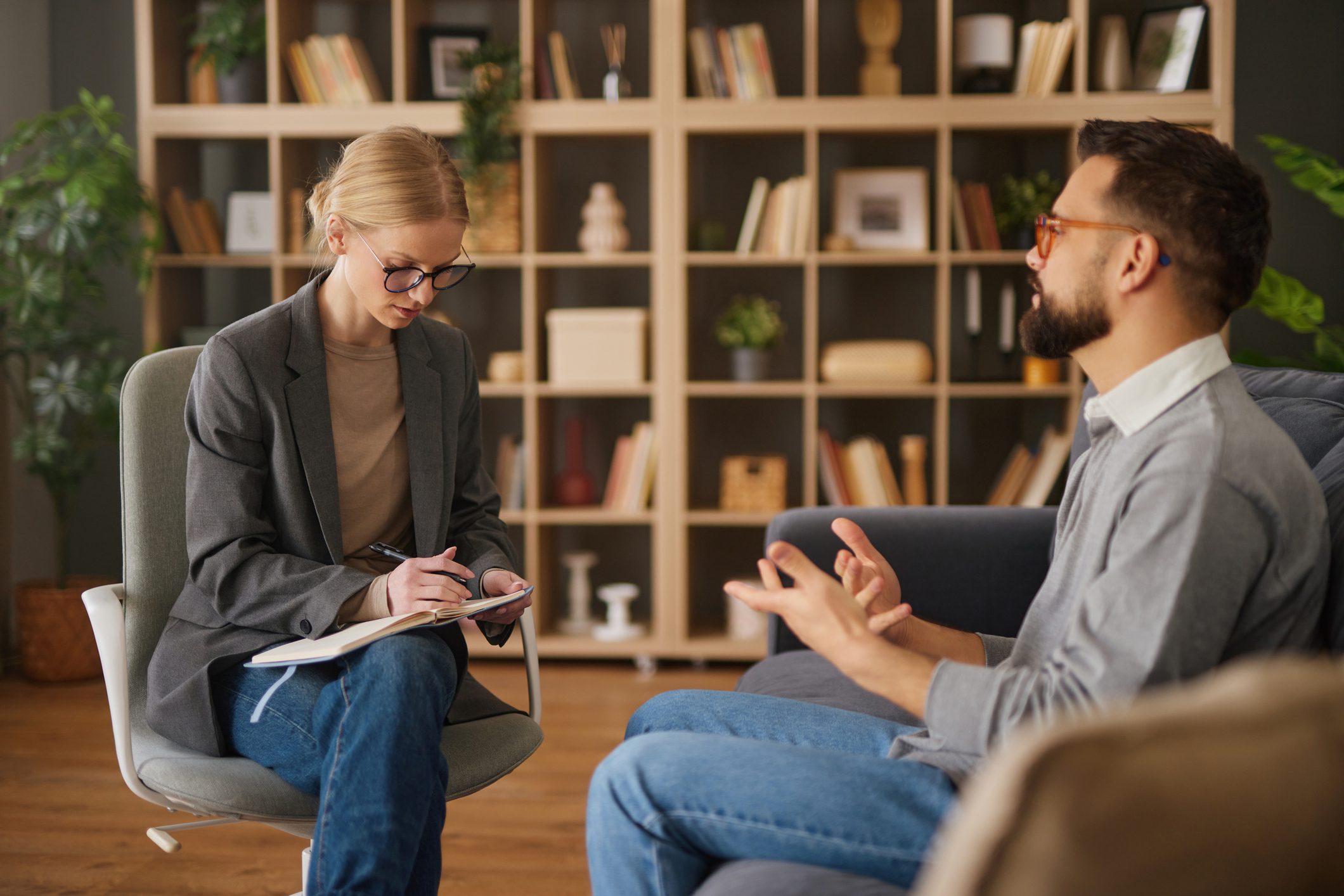 Female therapist writing notes while listening to a male patient expressing feelings during a consultation